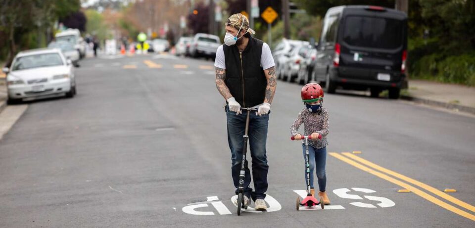 An adult and child use scooters on an open street.