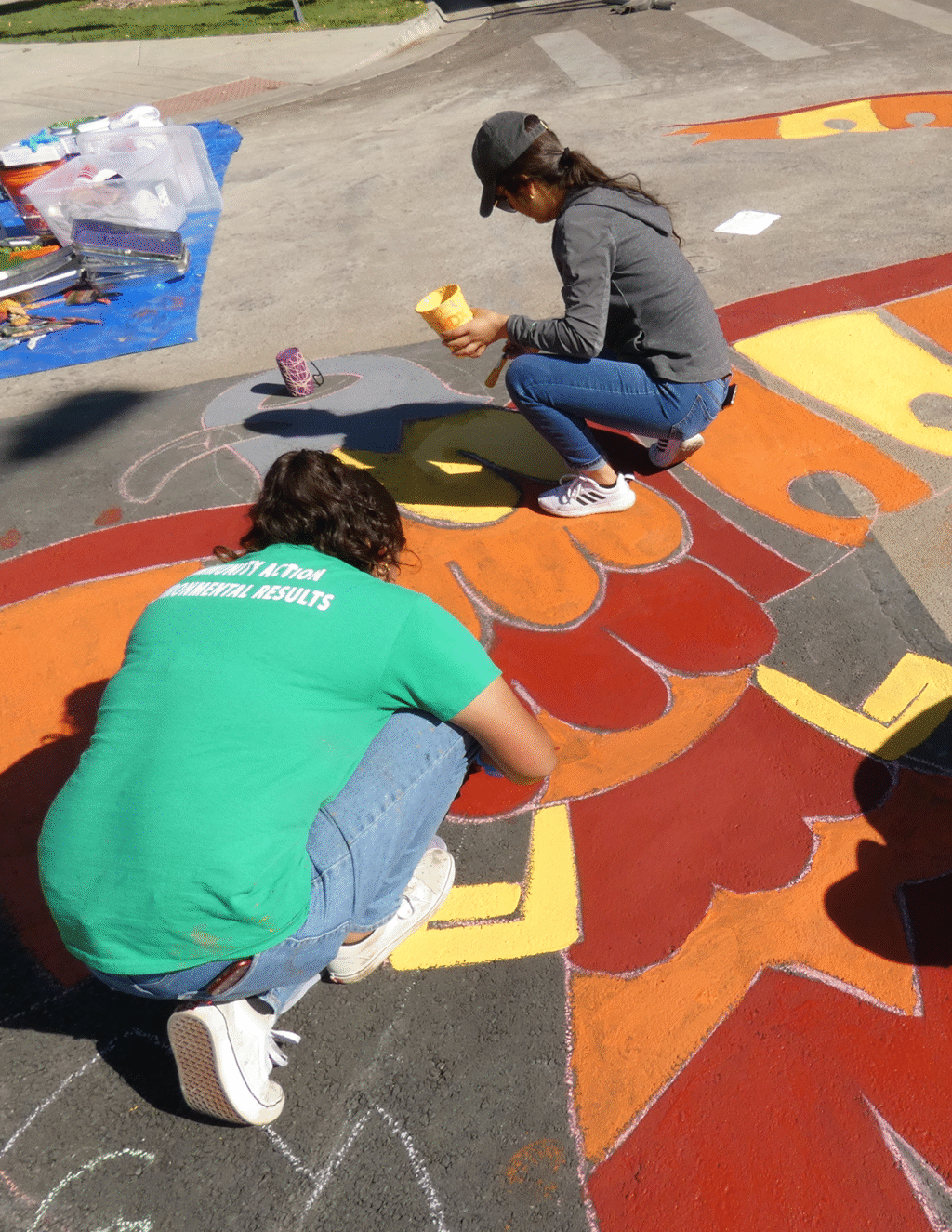 People work on a mural being painted in the roadbed of a street in Denver.