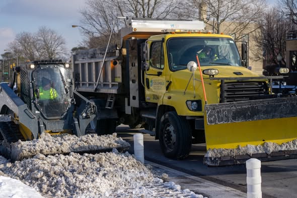 A small snow plow removes snow from a bike lane next to a larger truck plowing a vehicle lane in Columbus Ohio.