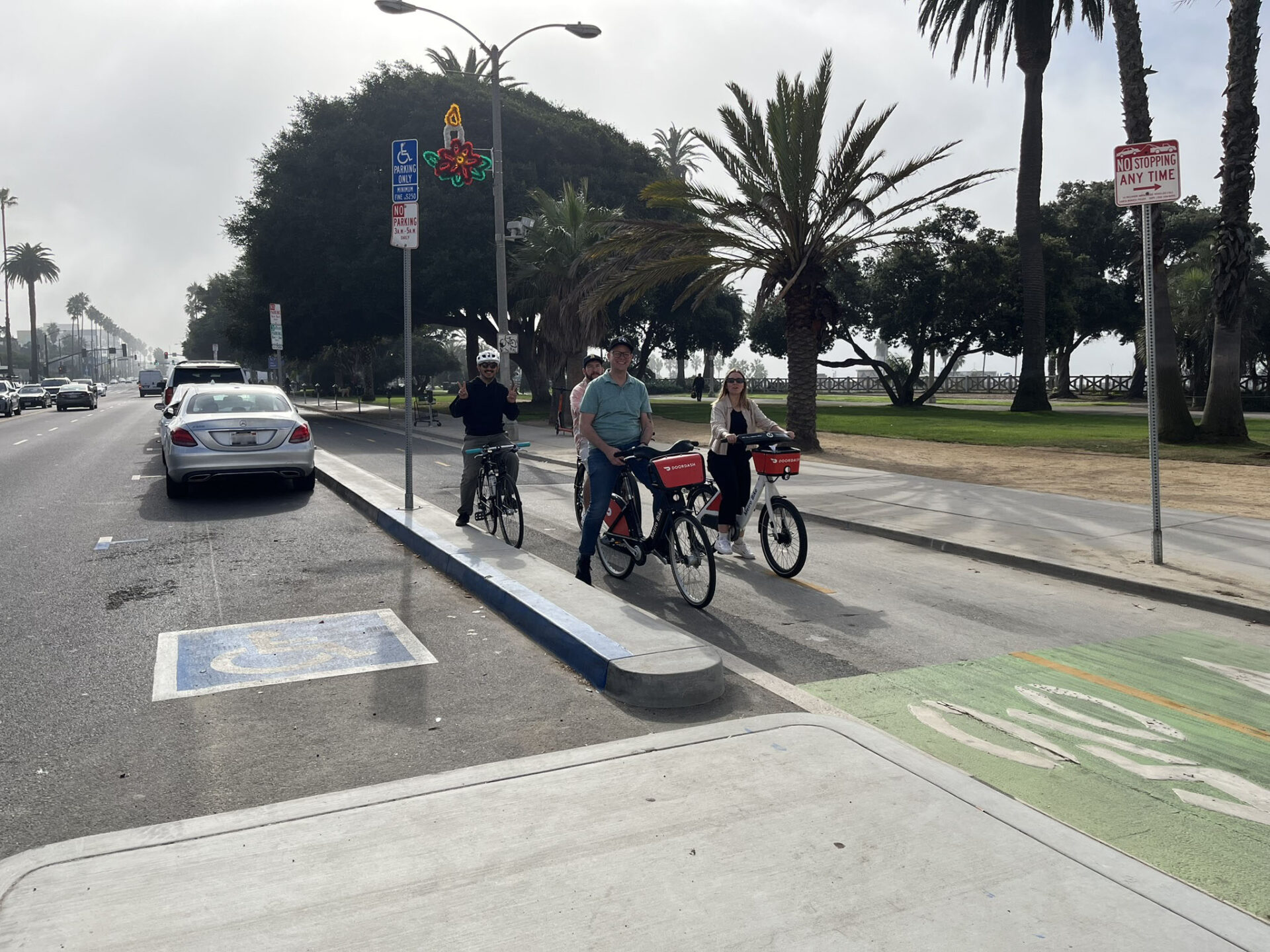 Four people on bikes in a protected bike lane adjacent to an accessible parking space.