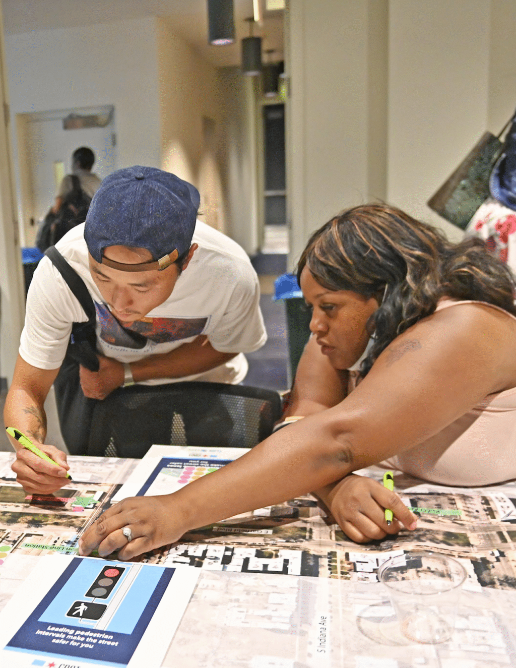 People gathered at a table covered in maps to write down their feedback on a project.