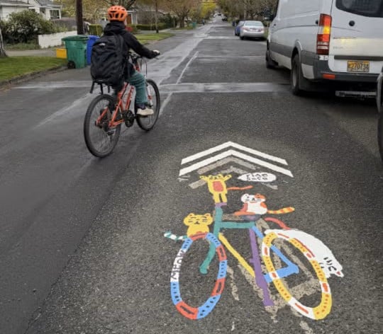 A custom-designed shared lane marking features a colorful bike and three cartoon cats.