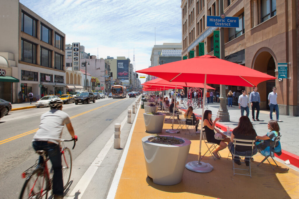 People sit under bright umbrellas at an in-street public plaza