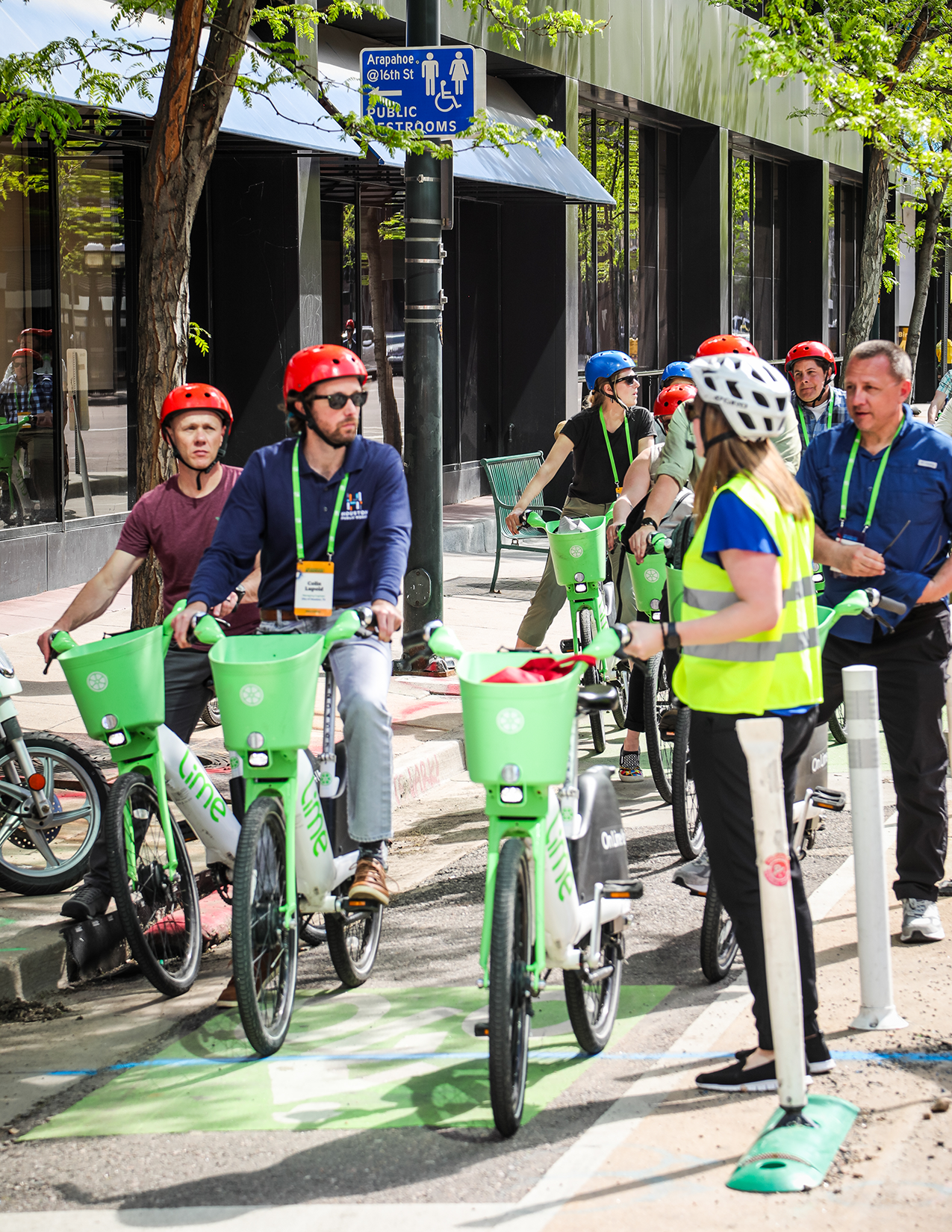 A group of people on Lime e-bikes wait in a bike lane and listen to a tour guide during a bike tour at the Designing Cities Conference in Denver, Colorado.