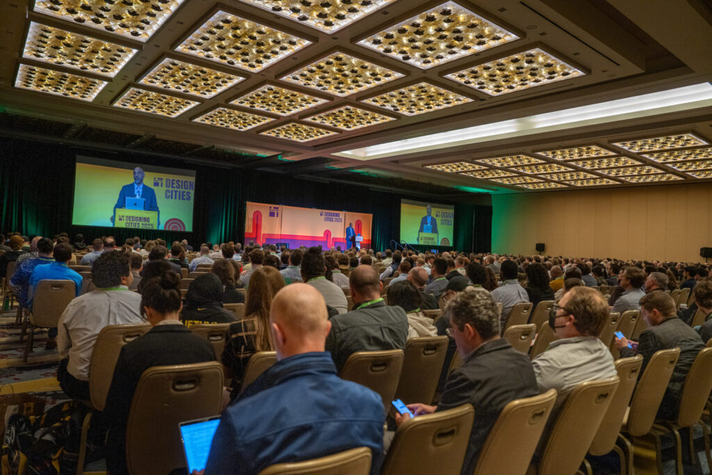 A crowded auditorium listens to NACTO President Mike Carrol speak at Designing Cities 2025