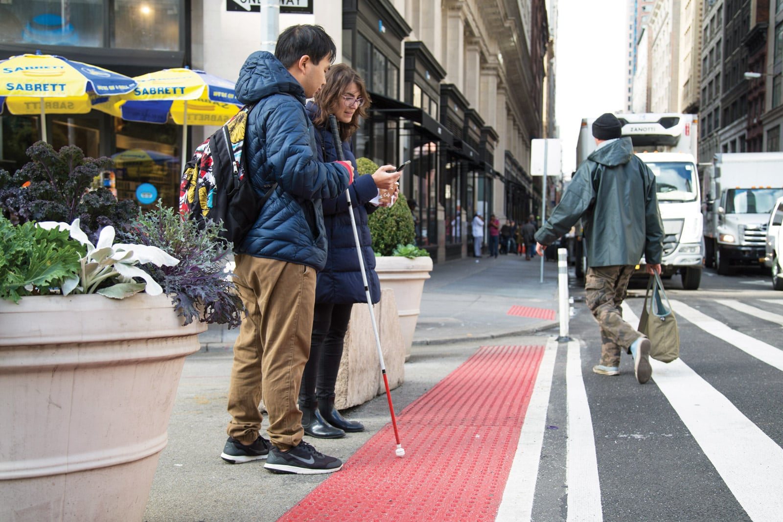 A person with a cane stands at a tactile strip next to a bikeway in NYC