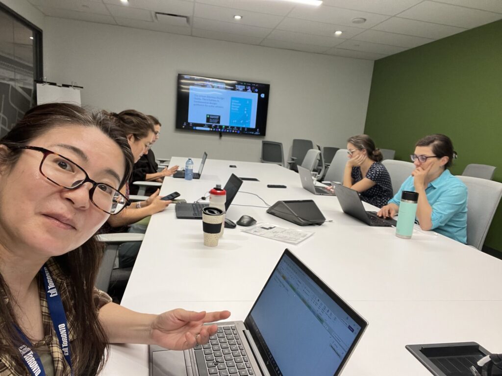 Five City of Toronto staff members sit at a conference table. A television displaying the bike guide Zoom training is in the background.