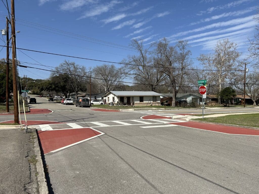 At a stop-controlled intersection, white lines and dark red surface treatment create sidewalk extensions at marked crosswalks.