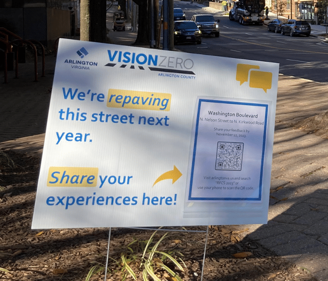 A yard sign features Arlington County's Vision Zero logo and says "We're repaving this street next year. Share your experiences here!" A paper flyer is taped to the sign and features a QR code.