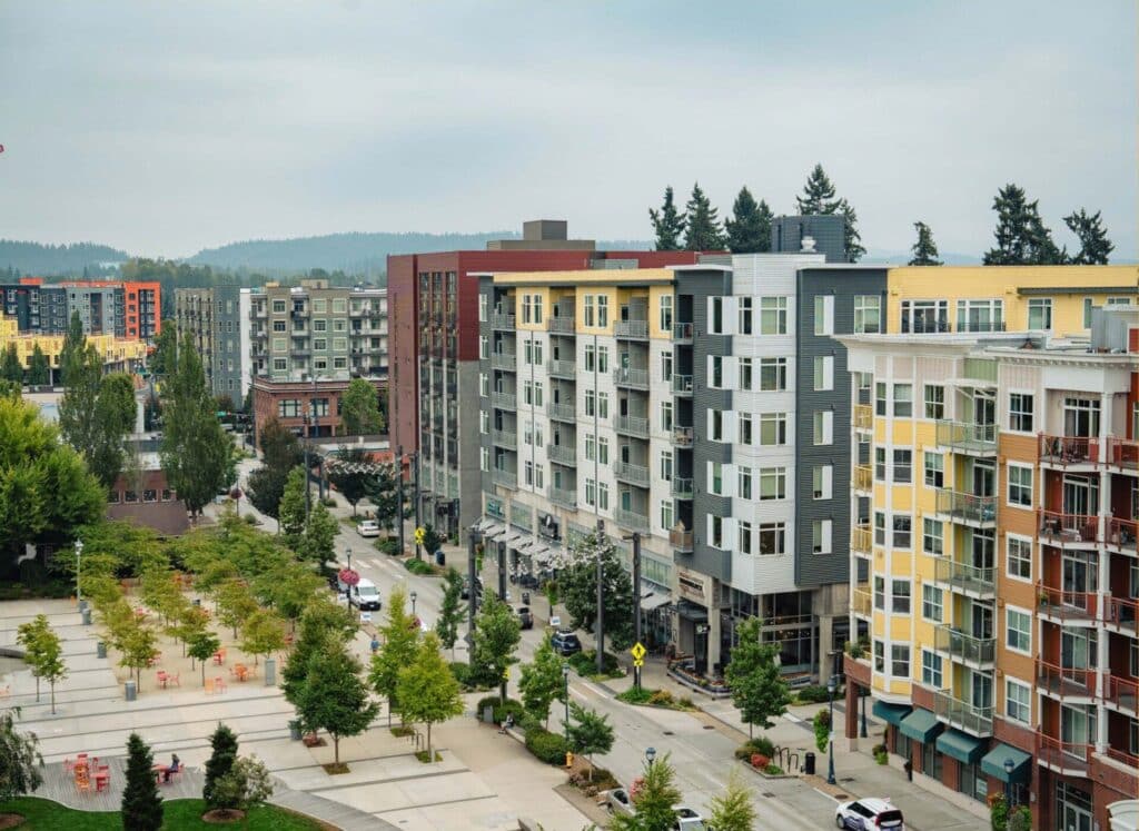 A photo of Redmond shows a series of mixed-use buildings across a two-lane street from a large plaza with tree plantings and movable orange chairs and tables.