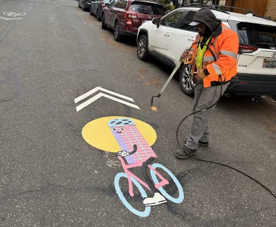 A staff member installs a custom shared lane marking that looks like a building riding a bike.