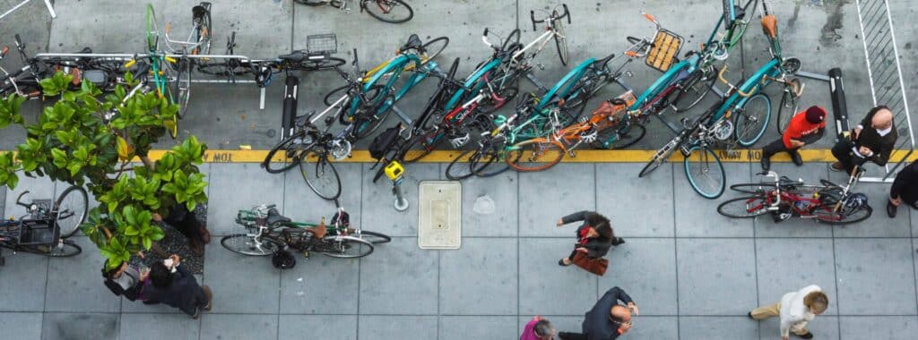 An overhead view of people walking on a sidewalk. Bikes are parked at bike racks in the curb lane.