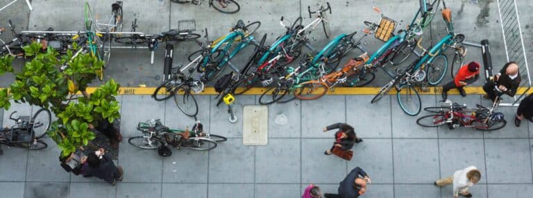 An overhead view of people walking on a sidewalk. Bikes are parked at bike racks in the curb lane.