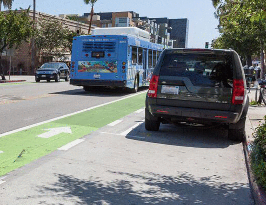 A vehicle is parked between the curb and a green bike lane. A bus is in the travel lane.