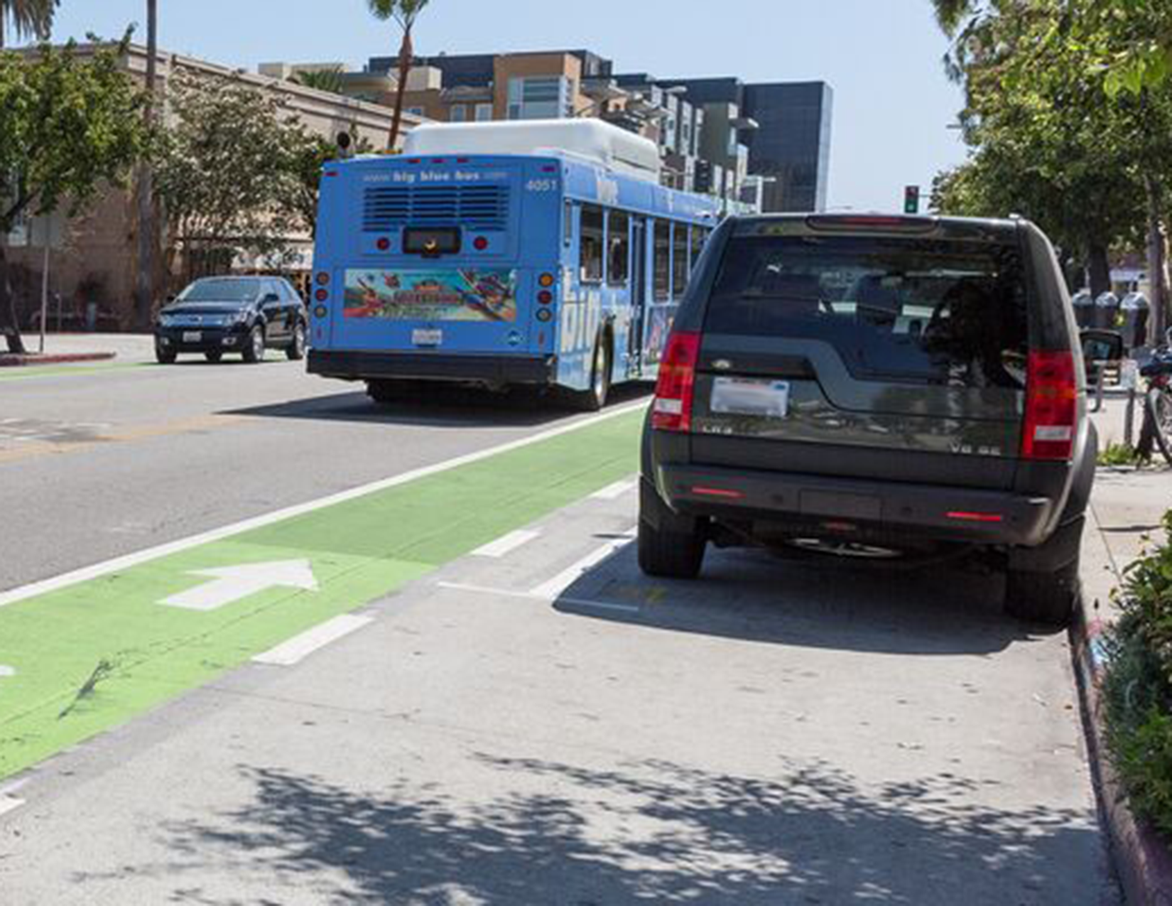 A vehicle is parked between the curb and a green bike lane. A bus is in the travel lane.